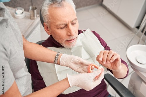 Doctor holding dentures or artificial teeth for man