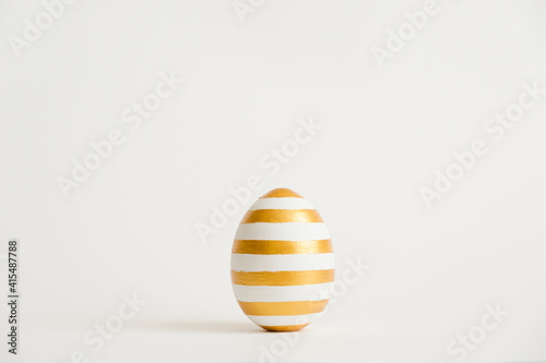 Easter golden with striped patternd egg isolated on white background. Minimal easter concept. Happy Easter card with copy space for text. Top view, flatlay. Concept for banner, flyer, invitation photo