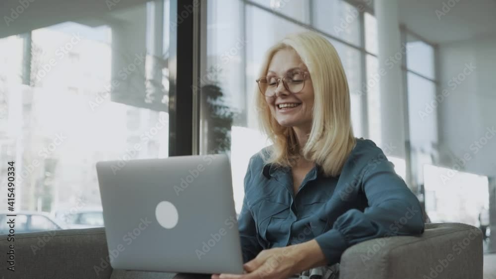 Smiling mature woman making video call using laptop, sitting on the couch Smiling mature woman making video call using laptop, sitting on the couch