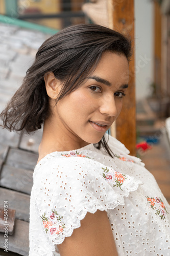 face of beautiful latin woman with short hair standing on the edge of a terrace, wearing a blouse with embroidery and prints