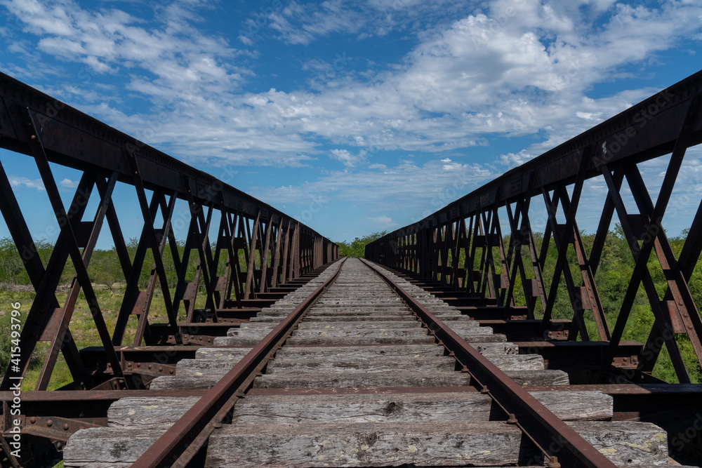 Abandoned iron railway bridge over a stream with a sky and clouds background