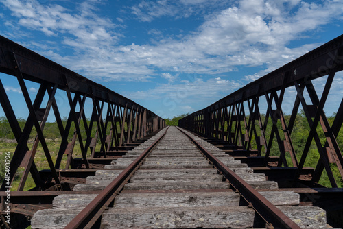 Abandoned iron railway bridge over a stream with a sky and clouds background © Carlos G. Baquero