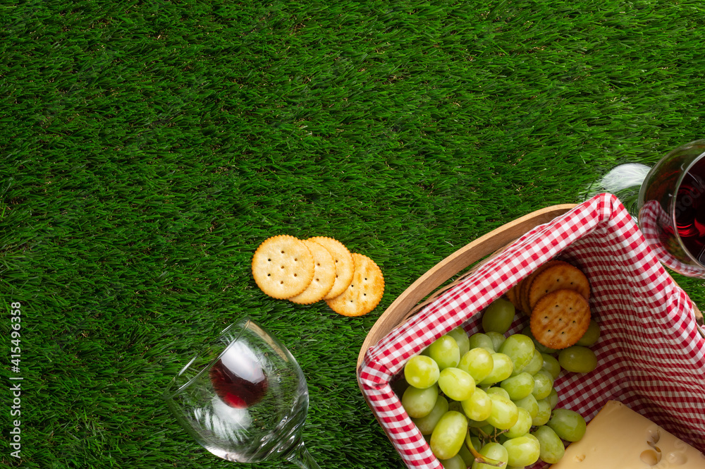 Naklejka premium Picnic and relaxation, picnic basket, glass with red wine and grapes and snacks. Top view on the grass with space for advertising. Banner