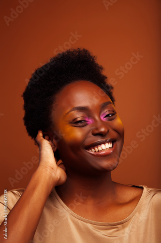 pretty young african american woman with curly hair posing cheerful gesturing on brown background, lifestyle people concept