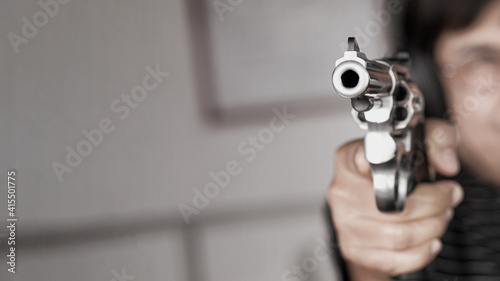 Woman pointing a gun at the target. Close-up image of the muzzle of a gun on dark background, vintage color tone.