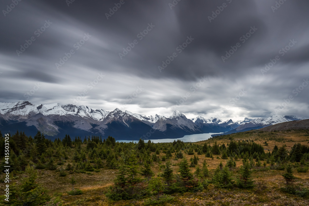 Long exposure of a Canadian Rockies landscape with a lake next to mountains with snow during autumn under a looming overcast sky with fast dark clouds, Maligne Lake, Jasper National Park, Canada Long exposure of a Canadian Rockies landscape with a lake next to mountains with snow during autumn under a looming overcast sky with fast dark clouds, Maligne Lake, Jasper National Park, Canada