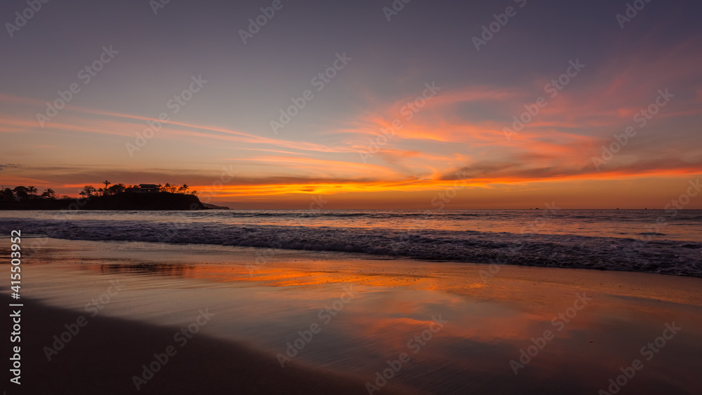 Tropical summer calm sunset landscape at the beach with sand, water, ocean waves, sky with orange curved clouds reflected on the sand, Flamingo Beach, Guanacaste, Costa Rica
