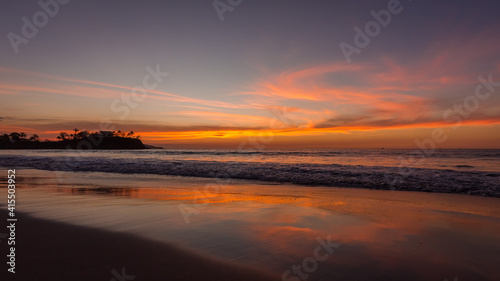 Tropical summer calm sunset landscape at the beach with sand, water, ocean waves, sky with orange curved clouds reflected on the sand, Flamingo Beach, Guanacaste, Costa Rica