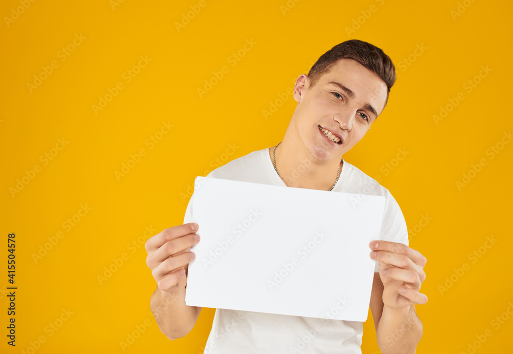 A man in a white T-shirt with a sheet of paper on a yellow background Copy Space mockup A man in a white T-shirt with a sheet of paper on a yellow background Copy Space mockup