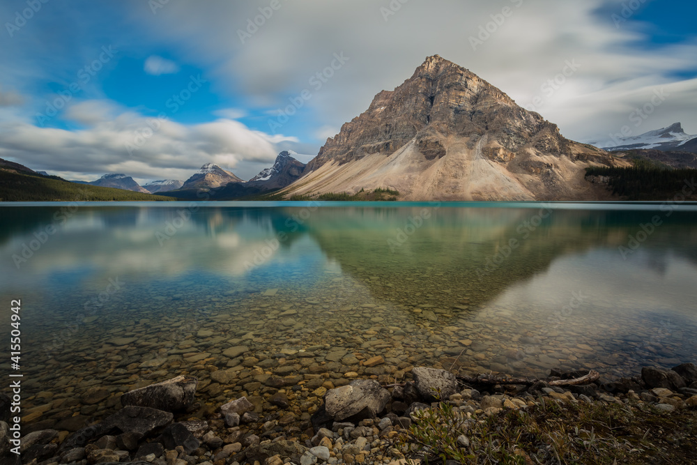 Rocky mountain reflected on clear smooth lake water with green and blue ...