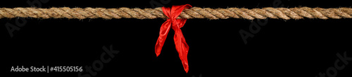 Long tug of war rope pulled tight, with red ribbon tie. Concept of conflict, competition, or rivalry. Isolated on black.