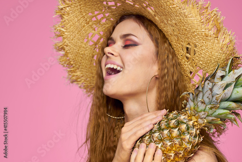 Woman with a gun in hands of a straw hat bright makeup exotic fruits summer pink background