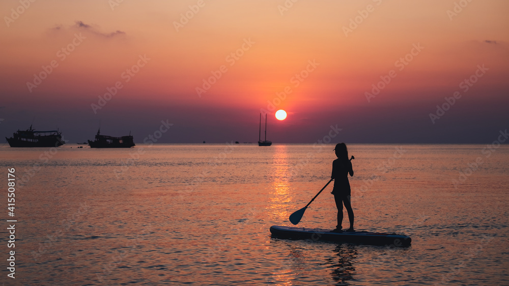 Silhouette image of a young woman on stand up paddle board in a sea before sunset