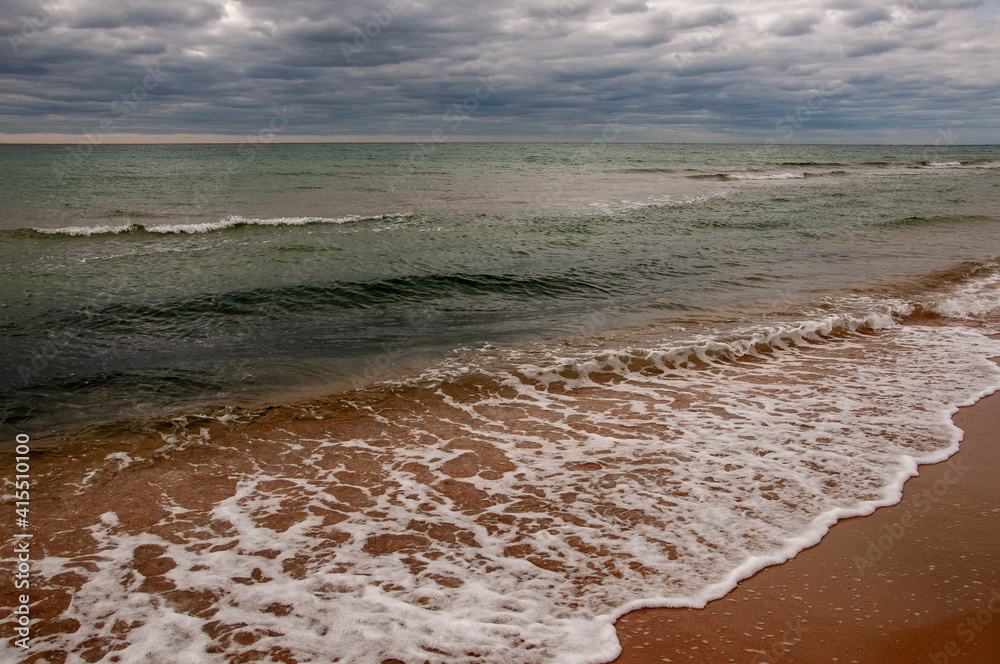 Fototapeta premium Black Sea. Water with waves. Dark cloudy weather. Deep bright blue water. Before storm. Sand coast