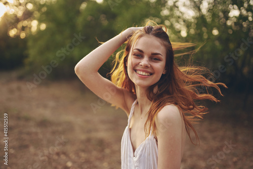 romantic woman in a dress gestures with her hands outdoors near green trees