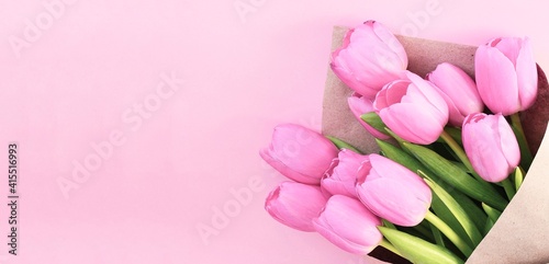 Fototapeta Naklejka Na Ścianę i Meble -  Bouquet of tulips wrapped in craft paper on pink background with space for text. Greeting card. Concept woman's or mother's day. Spring flowers background. Banner