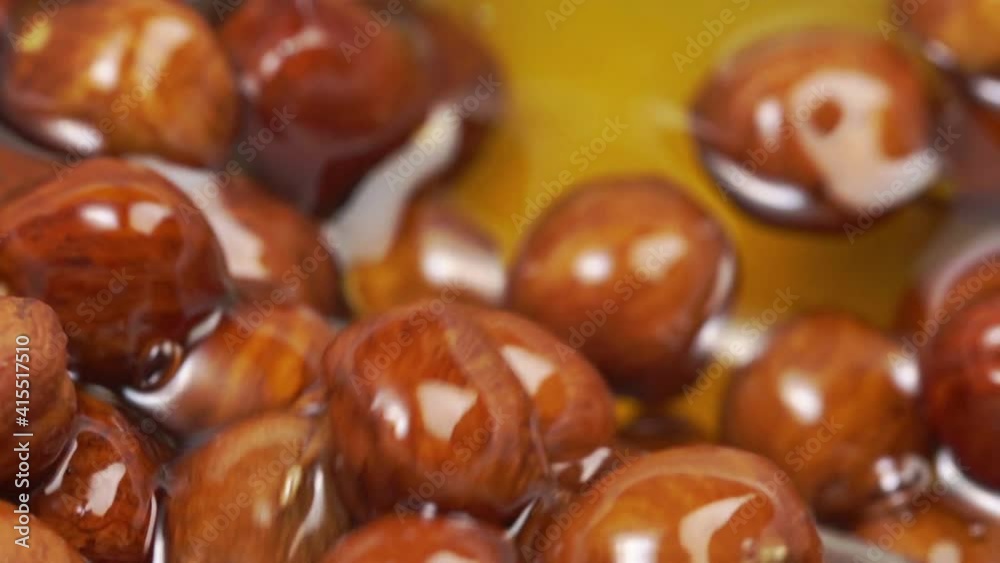 Honey pouring into bowl of hazelnuts in slow motion.