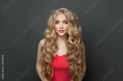 Cute blonde woman with long curly hair in red dress on black