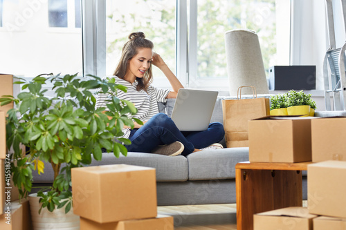 Obraz na plátně Young woman sitting on the sofa using laptop while moving in to new apartment