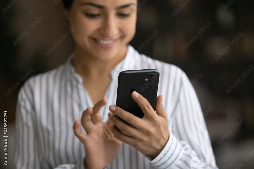 Crop close up of smiling Indian woman hold cellphone text or message using wireless internet connection. Happy mixed race female user browse web on modern smartphone gadget. Technology concept. Crop close up of smiling Indian woman hold cellphone text or message using wireless internet connection. Happy mixed race female user browse web on modern smartphone gadget. Technology concept.