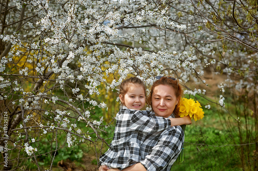 Mother and daughter on the background of flowering trees on a spring walk Mother and daughter on the background of flowering trees on a spring walk