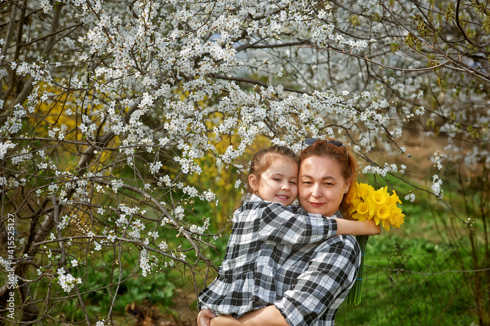 Mother and daughter on the background of flowering trees on a spring walk Mother and daughter on the background of flowering trees on a spring walk
