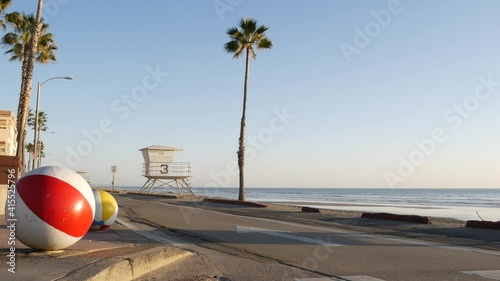 Pacific ocean beach, Oceanside California USA. Ball, lifeguard tower, life guard watchtower hut and tropical palm tree, sky, beachfront street, waterfront road. Los Angeles vibes, aesthetic atmosphere