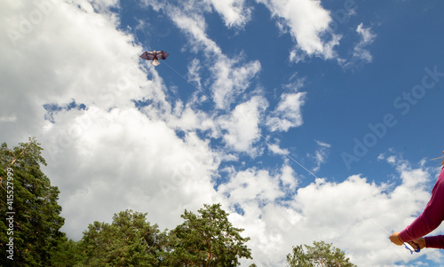 Hands hold a rope with a kite in the blue sky