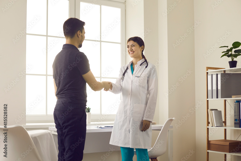 Obraz premium Healthcare and medicine. Friendly smiling female doctor greets and shakes hands with male patient during meeting in medical office. Concept of partnership, trust and medical ethics.