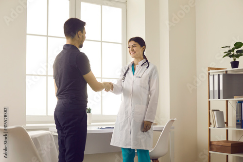 Healthcare and medicine. Friendly smiling female doctor greets and shakes hands with male patient during meeting in medical office. Concept of partnership, trust and medical ethics.