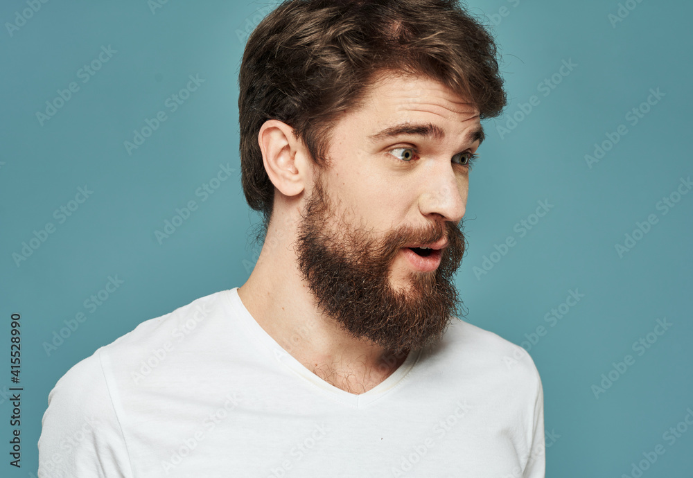Portrait of an emotional man in a white t-shirt on a blue background and a thick beard mustache model Portrait of an emotional man in a white t-shirt on a blue background and a thick beard mustache model