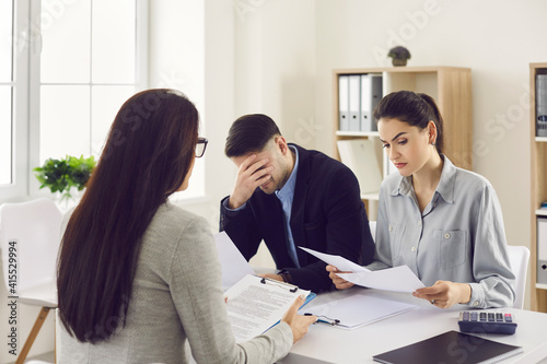 Bank worker or loan broker giving bad news to clients. Sad couple sitting at office table reading letter informing of bankruptcy or unprofitable investment. Property law and serious finance problems photo