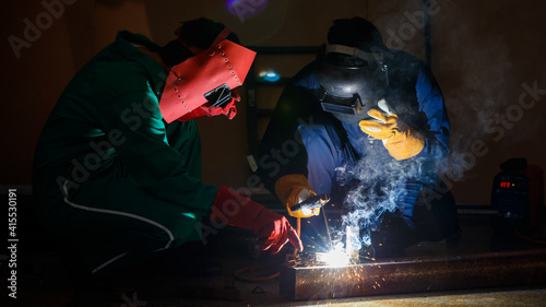 mechanics workers work overtime hardly at night in a factory. Engineers wearing safety outfits with mechanic jumpsuits, gloves, boots, and welding helmets working on metal welding