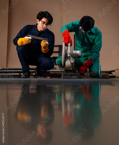 two smart Asian engineers wearing a mechanic jumpsuit, safety glasses, and glove sitting and holding tools posing smiling to a camera for photographing frow low angle view photo