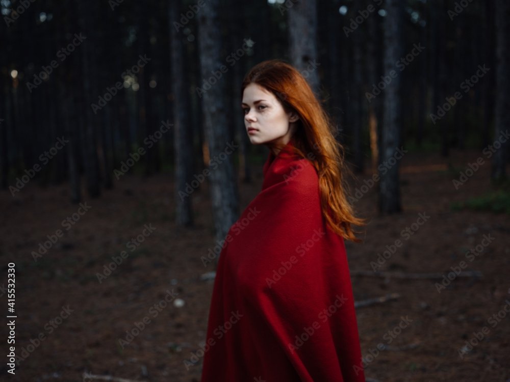A red-haired woman with a plaid on her shoulders walks in the forest near the trees A red-haired woman with a plaid on her shoulders walks in the forest near the trees