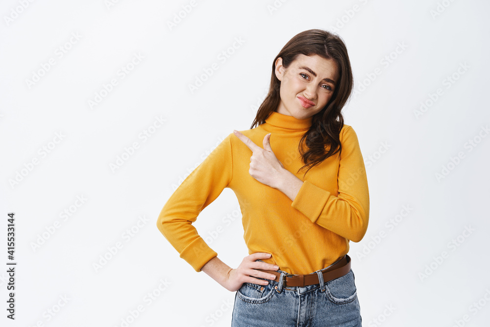 Skeptical girl express dislike and doubts, grimacing over bad promotion, pointing finger left at empty space for banner, white background
