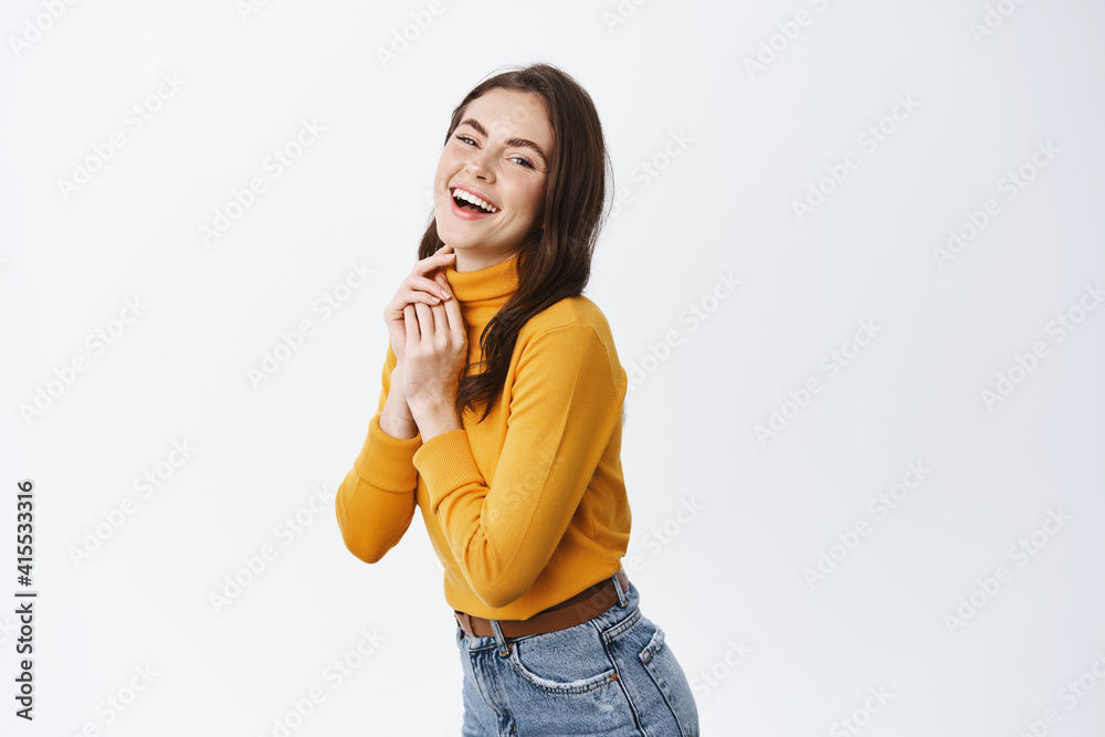 Happy beautiful woman in yellow sweater, laughing and expressing positive emotions, smiling at camera, standing half-turned on white background Happy beautiful woman in yellow sweater, laughing and expressing positive emotions, smiling at camera, standing half-turned on white background