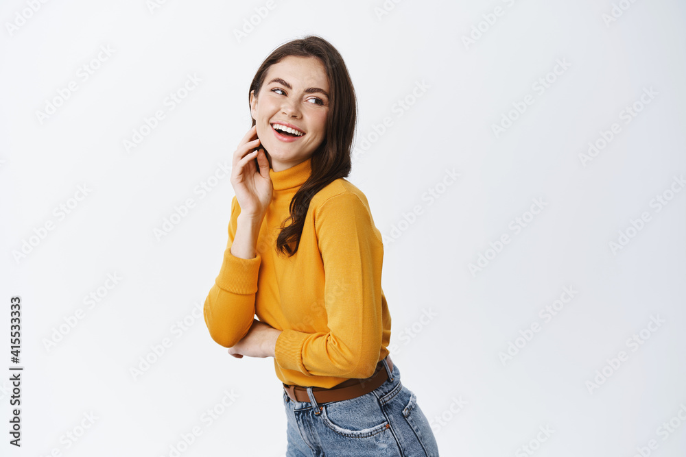 Beauty and fashion concept. Happy young woman look behind at empty space and laughing, touching face with natural light make up, standing against white background Beauty and fashion concept. Happy young woman look behind at empty space and laughing, touching face with natural light make up, standing against white background