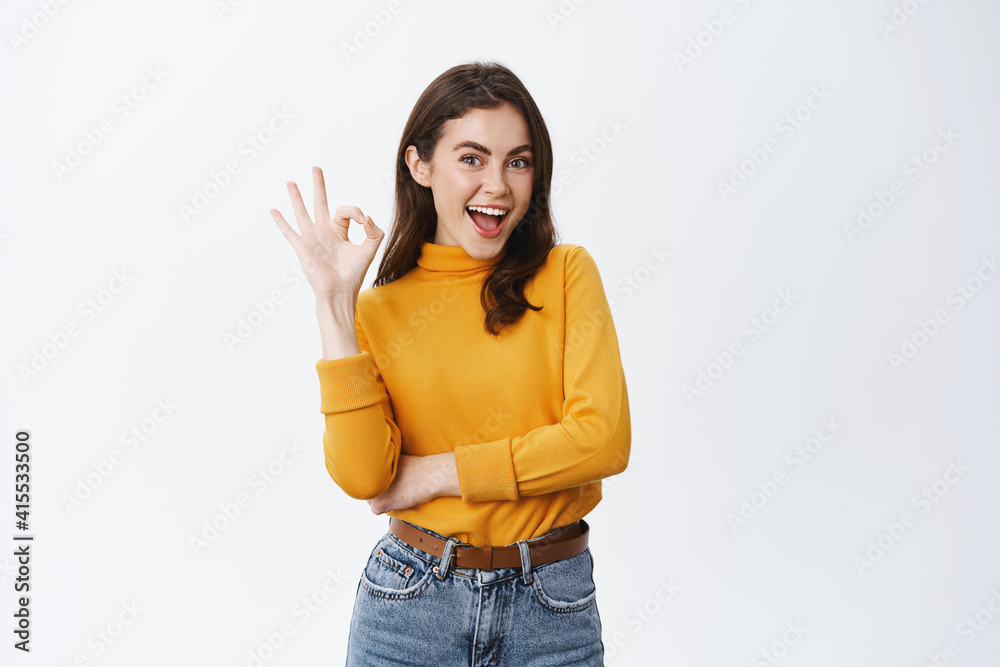 Very good. Smiling young female model with natural make up, showing okay sign and say yes, confirm product is alright, approve and like something, standing on white background Very good. Smiling young female model with natural make up, showing okay sign and say yes, confirm product is alright, approve and like something, standing on white background