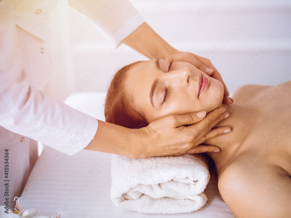Beautiful brunette woman enjoying facial massage with closed eyes in sunny spa center . Relaxing treatment and cosmetic medicine concepts Beautiful brunette woman enjoying facial massage with closed eyes in sunny spa center . Relaxing treatment and cosmetic medicine concepts