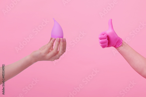 Hands of a young woman in pink latex gloves and hand with menstrual cup on pink background. women's health. preservation of ecology. waste-free use. women's hygiene products