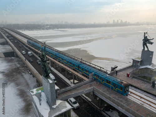 The Kiev metro train travels across the bridge through the Dnieper river. Aerial drone view. Winter sunny morning.