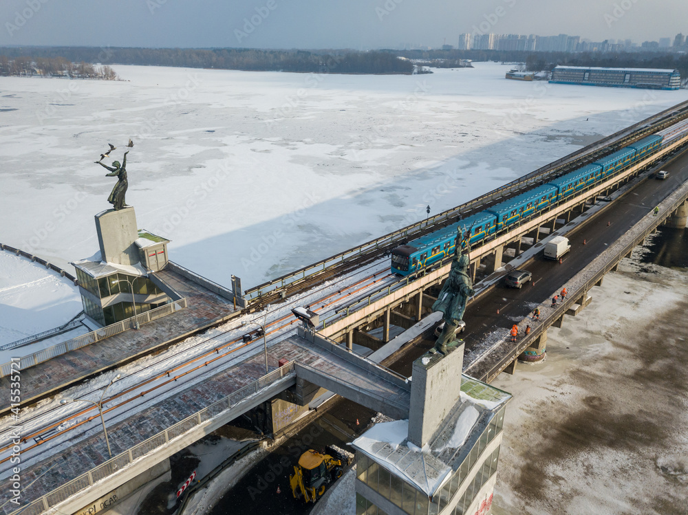 The Kiev metro train travels across the bridge through the Dnieper river. Aerial drone view. Winter sunny morning.