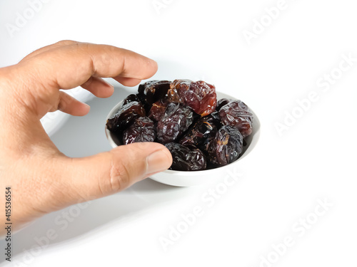 Selective focus.Hand holding dried sweet dates on bowl isolated on white background. Healthy food concept.
