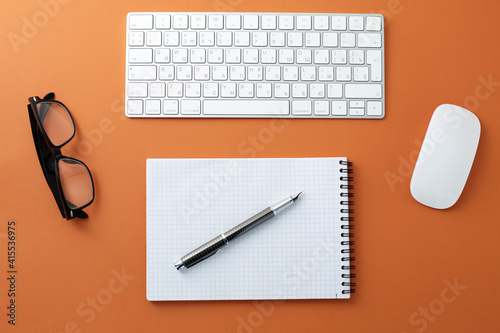 Glasses mouse keyboard notepad and pen on orange background
