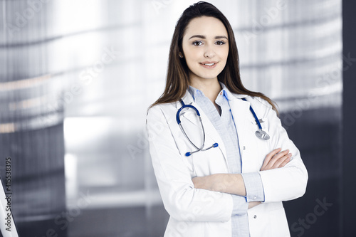 Young smiling woman-doctor is standing with arms crossed in a clinic office. Portrait of a friendly physician woman. Perfect medical service in a hospital. Medicine concept