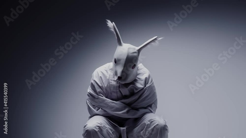 Mad man wearing rabbit mask in a white room. Mental disorder, psychosis concept. Schizophrenia and depression symbol. Masked, crazy person wearing straitjacket in a mental hospital.