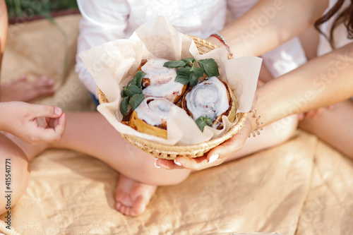Female hands holding out a basket of cinnabon buns. Dessert during a picnic.