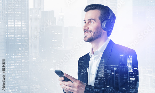 Young European man in elegant suit listening to music with headp