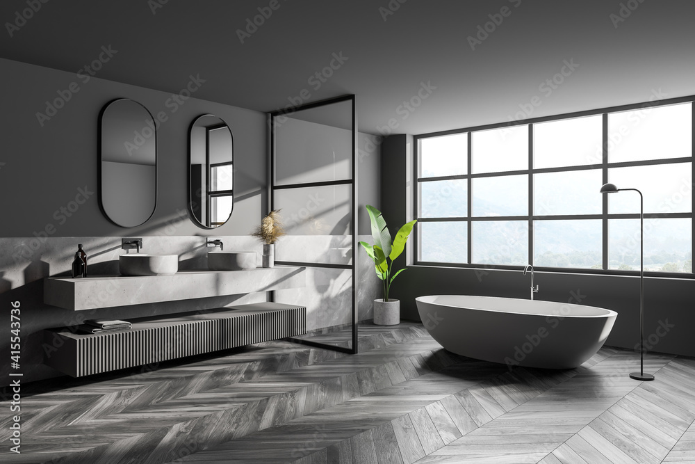 Interior of modern bathroom with grey walls, wooden parquet on floor, double sink with two mirrors above it and comfortable white bathtub.